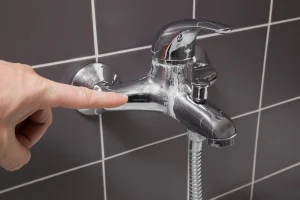 Man's hand finger pointing to calcified water tap in the bathroom.